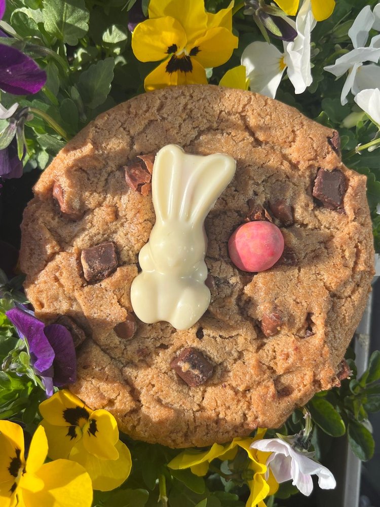A chocolate chunk cookie topped with a white chocolate bunny, surrounded by pansies