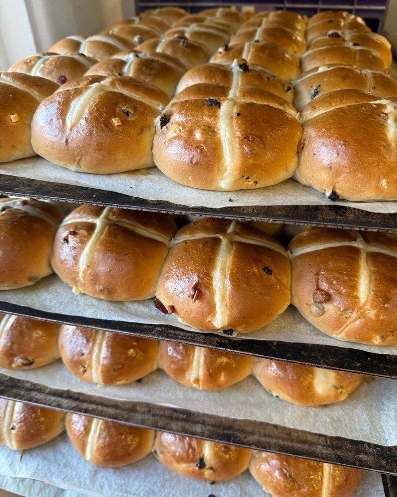 Trays of freshly baked hot cross buns cooling on racks